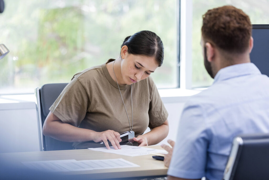 The mid adult female veteran signs paperwork with her banker present to ensure her accounts are set up correctly.